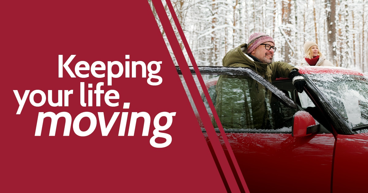 Smiling couple by red car in snow